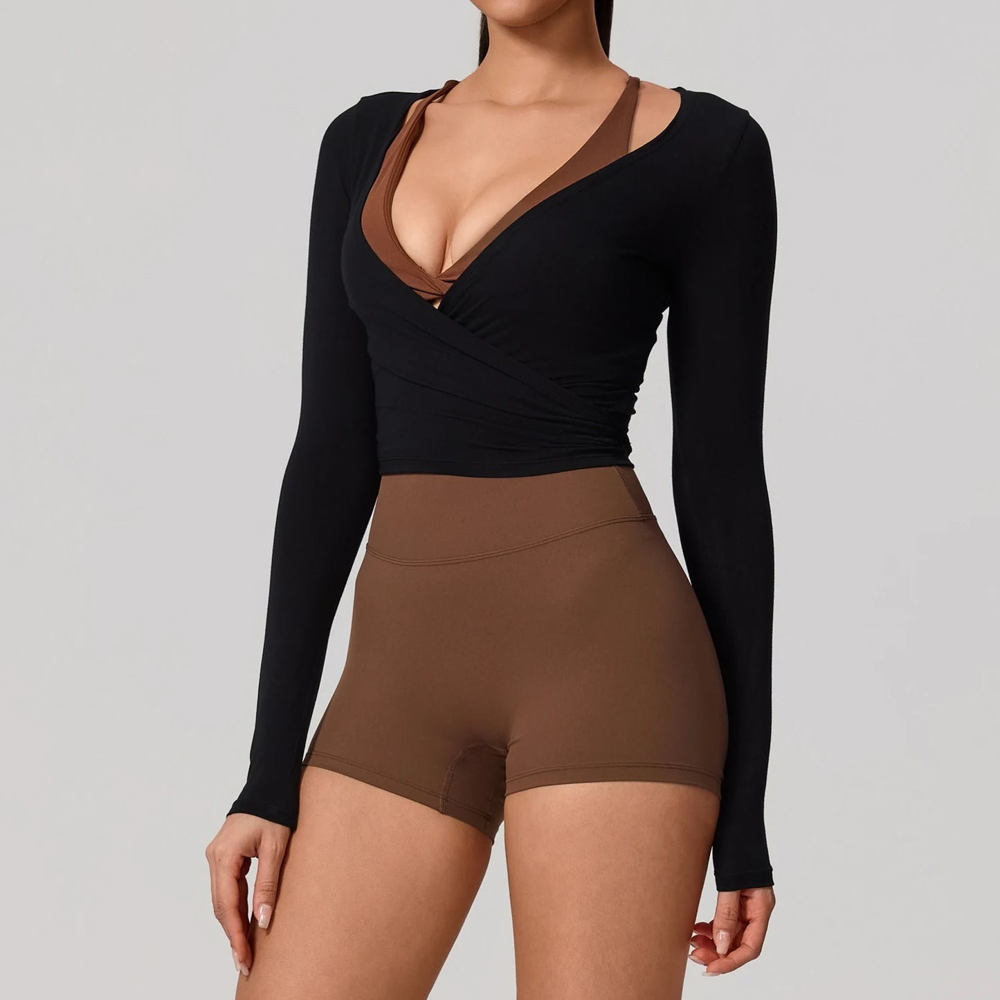 Long sleeve black wrap yoga shirt with V-neckline, styled casually with brown shorts for a chic, sporty look.