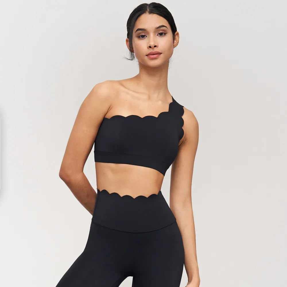 One-shoulder black yoga bra with scalloped edges, paired with high-waisted leggings, showcasing elegant activewear style.