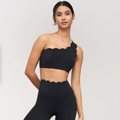 One-shoulder black yoga bra with scalloped edges, paired with high-waisted leggings, showcasing elegant activewear style.
