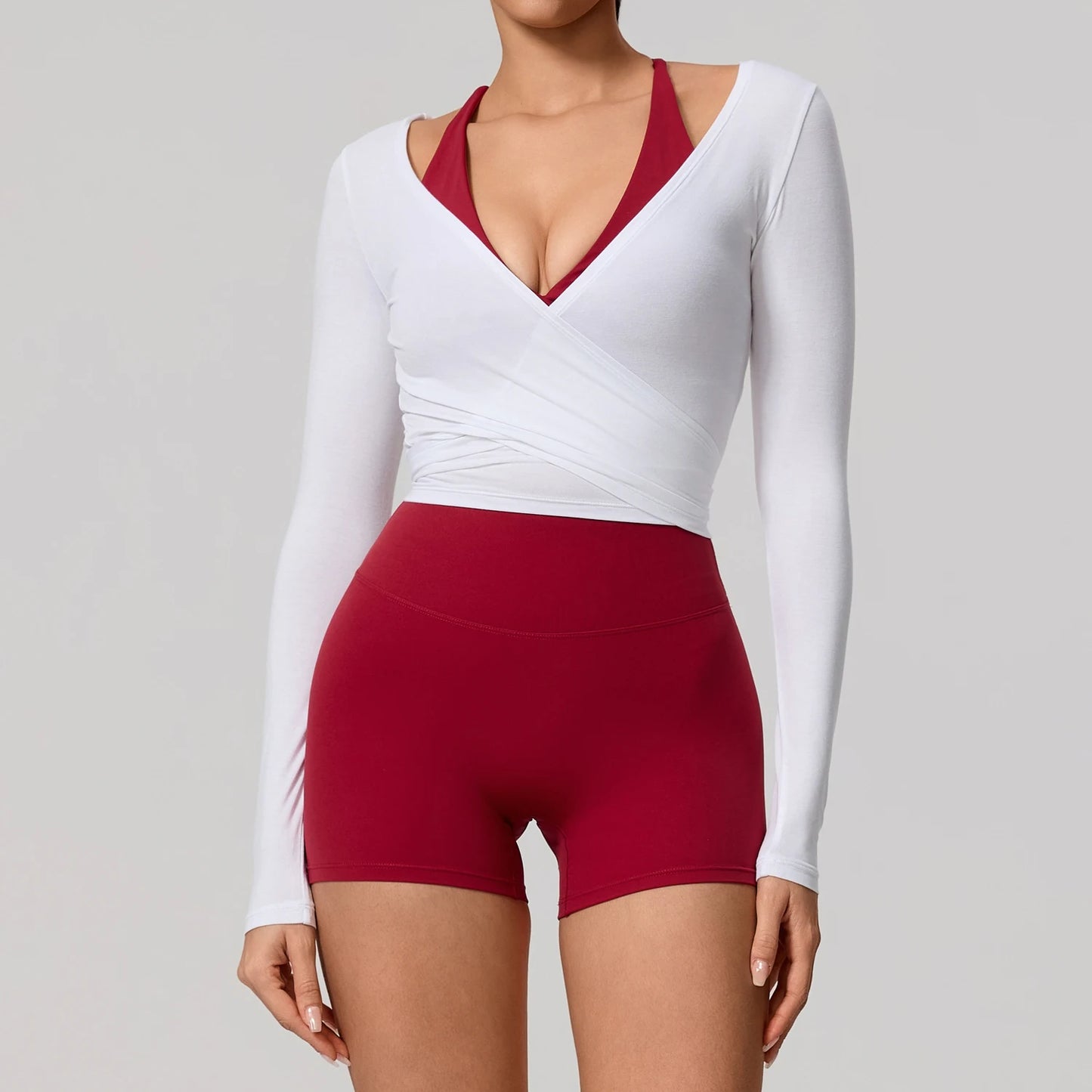 Long sleeve white wrap yoga shirt with a flattering V-neckline, styled with red sports bottoms.