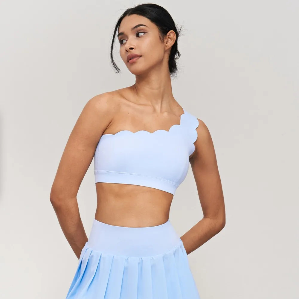 One-shoulder yoga bra with scalloped edges, elegantly styled in a light color, paired with a matching skirt.