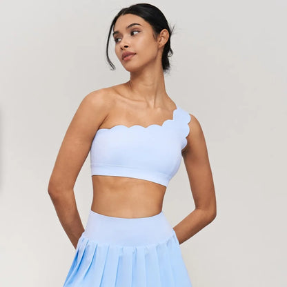 One-shoulder yoga bra with scalloped edges, elegantly styled in a light color, paired with a matching skirt.