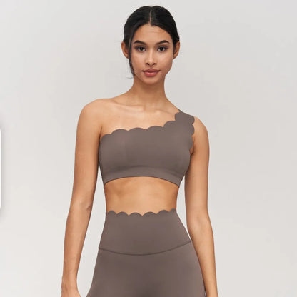 One-shoulder nude yoga bra with scalloped edges, paired with matching bottoms for a chic workout look.