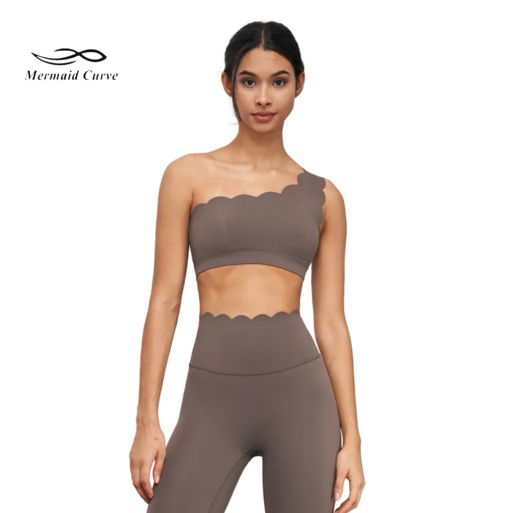 One-shoulder nude yoga bra with scalloped edges, paired with high-waisted leggings for a chic workout look.